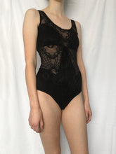 Load image into Gallery viewer, Side front view of size 8 tall white model wearing black lace cutout bodysuit stood in front of white fabric background.
